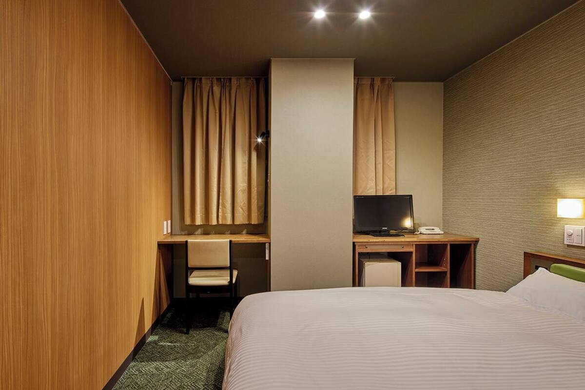 Ett hotellrum med en säng, ett skrivbord med en stol, en tv och en telefon.