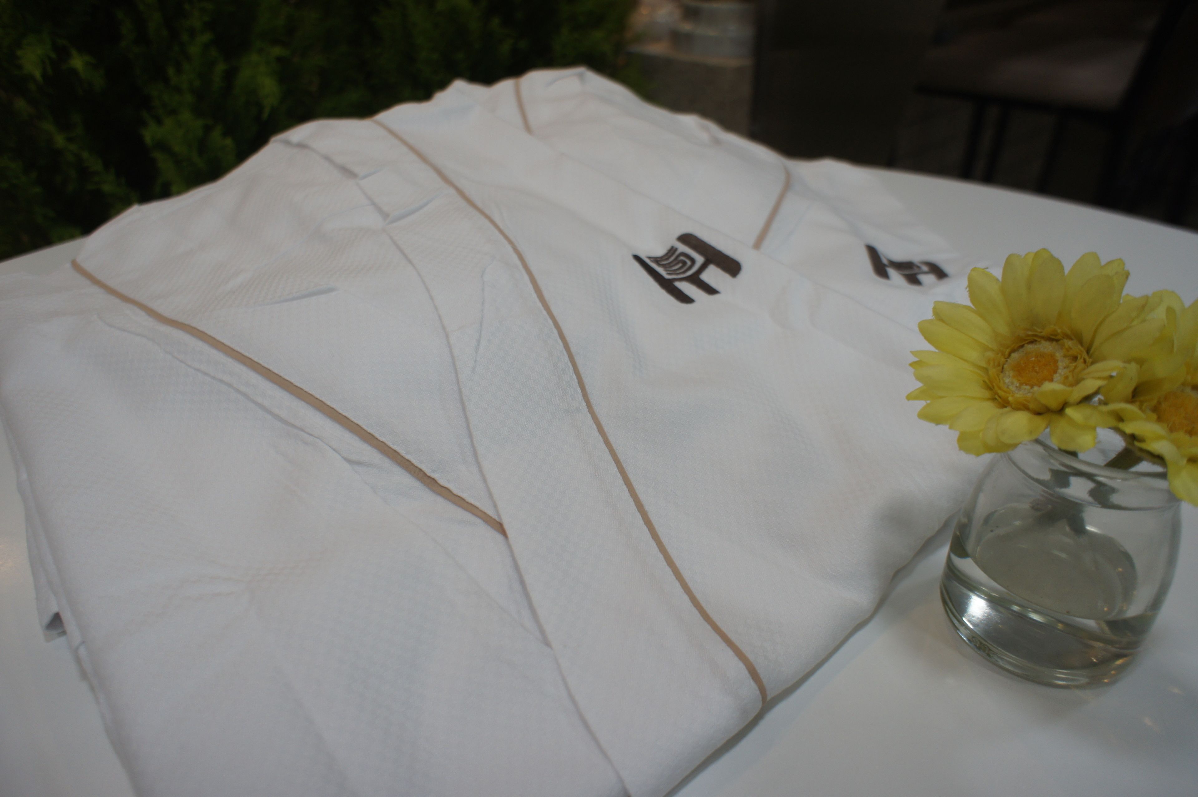A white shirt with a logo on it and a glass vase with yellow flowers on a table.