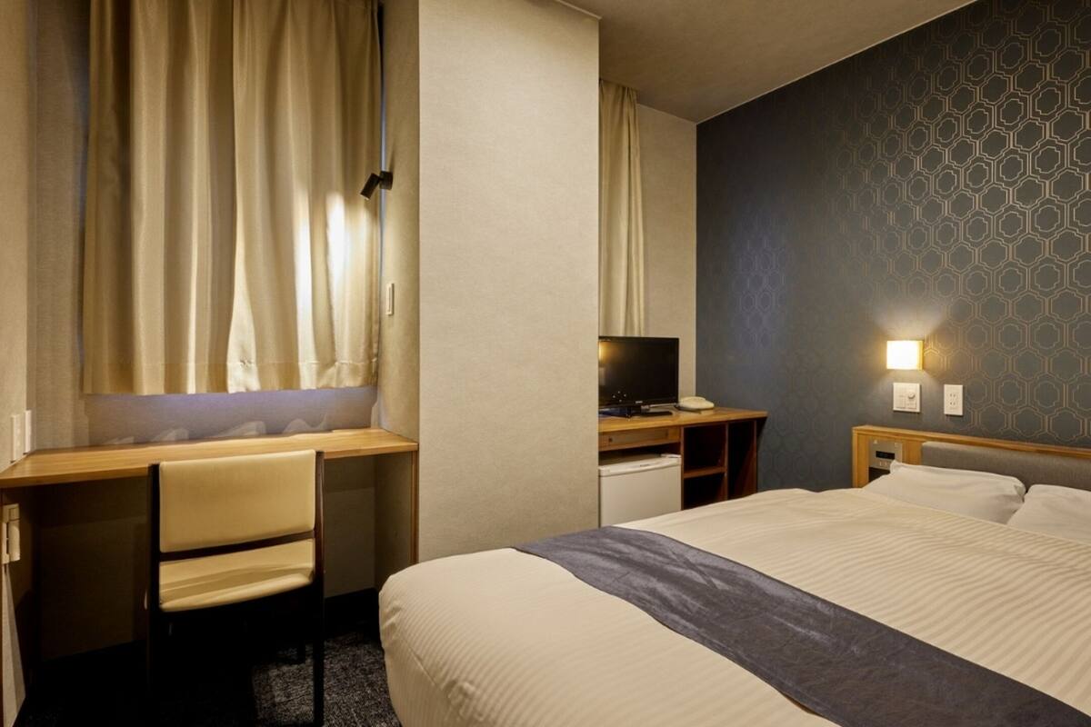 Ett hotellrum med en säng, ett skrivbord, en stol och en tv.