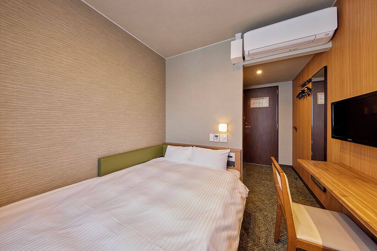 Ett hotellrum med en säng, ett skrivbord, en stol, en tv och en luftkonditioneringsanläggning.