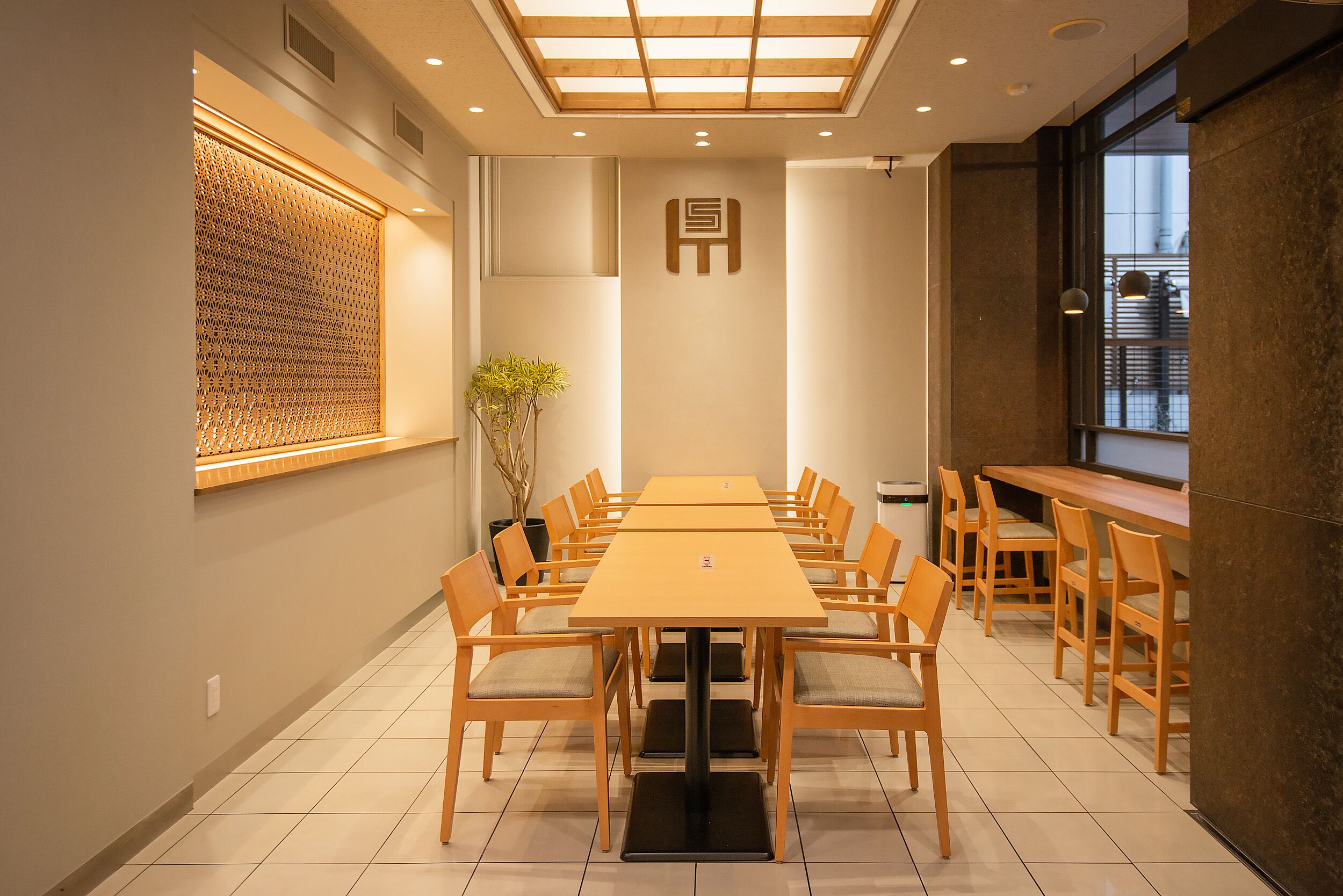 A conference room with a long table and chairs, a decorative wall panel, and a potted plant.