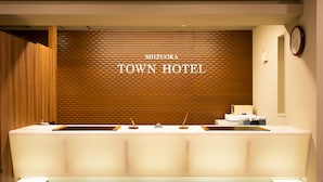 A reception desk at Shizuoka Town Hotel with a modern design, a clock on the wall, and a textured wall behind it. - Shizuoka Town Hotel (Shizuoka)