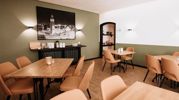 A dining area with wooden tables and chairs, a black and white cityscape painting on the wall, and a shelf with jars and a coffee pot. - Arcade Hotel Hamburg (Hamburg)