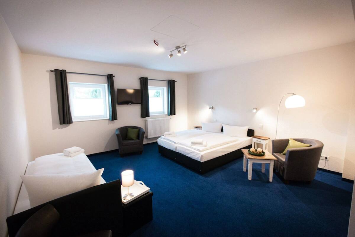 Habitación de hotel con una cama grande, un escritorio, una silla y una mesita de noche con una lámpara.