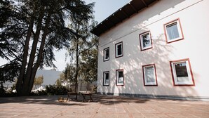 A building with a white exterior and red window frames, a paved courtyard with a bench, and a large tree providing shade. - Arcade Hotel Hamburg (Hamburg)
