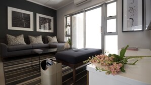 A modern living room with a grey sofa, patterned cushions, a coffee table, a trash bin, and a white desk with a vase of flowers. - Insignia Lifestyle (Sandton)