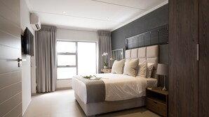 A modern bedroom with a large bed, a TV, a bedside table with a lamp, and a wardrobe. - Insignia Lifestyle (Sandton)
