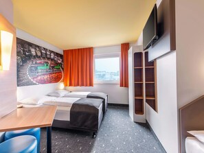 Une chambre d’hôtel avec un lit, un bureau, une chaise, une télévision et une fenêtre avec des rideaux.