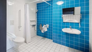 A bathroom with a white toilet, a shower with a white curtain, a sink with a mirror, and blue tiled walls. - B&B Hotel Augsburg-Süd (Augsburg)