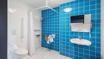 Een badkamer met een wit toilet, een douche met een witte gordijn, een wastafel met een spiegel en blauwe betegelde muren.