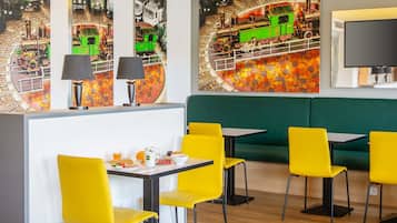 A restaurant with yellow chairs, a green booth, and a wall with a train mural.