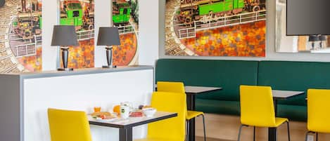A restaurant with yellow chairs, a green booth, and a wall with a train mural.