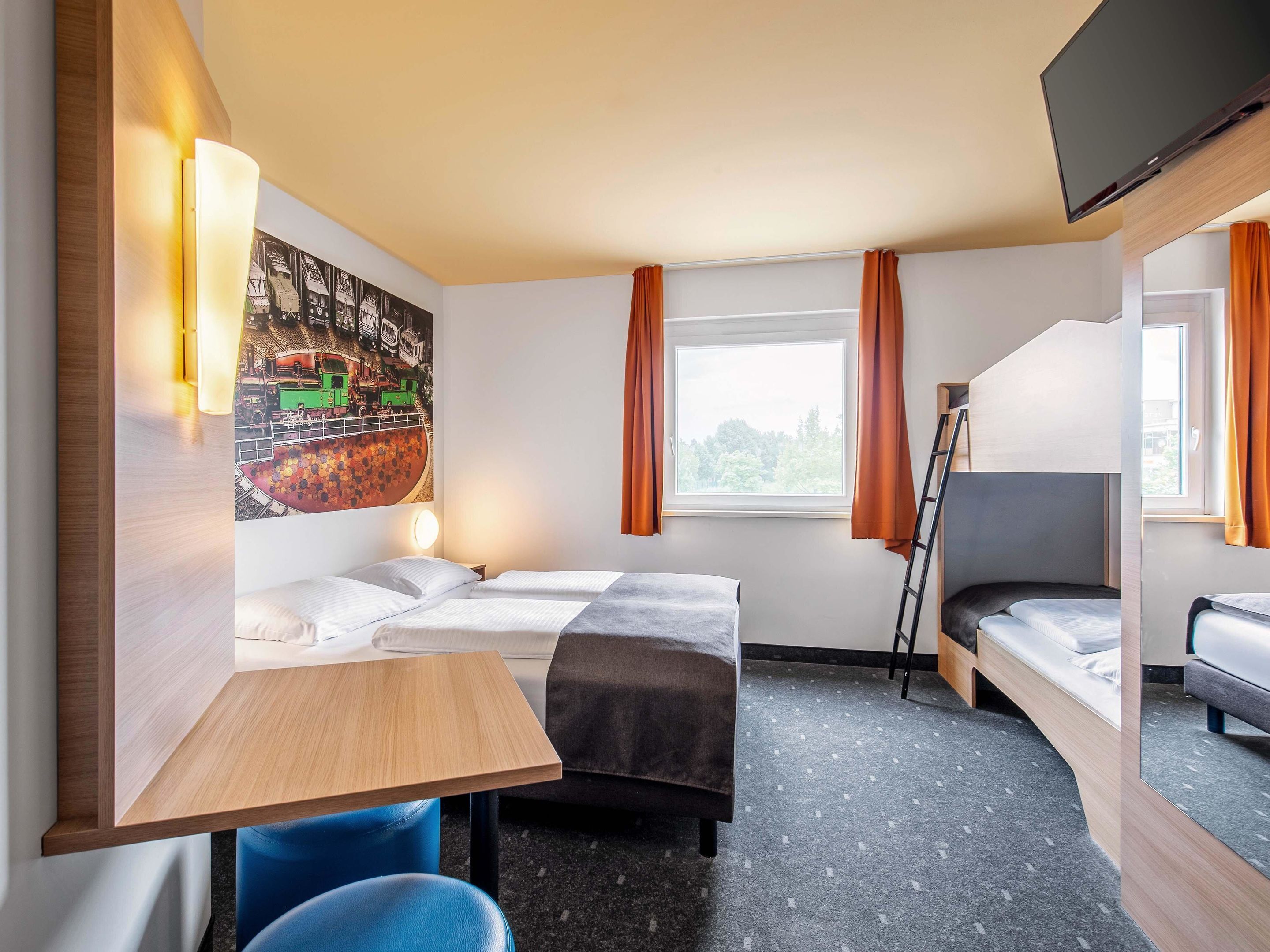 A hotel room with two beds, a desk, a chair, a TV, and a window with curtains.