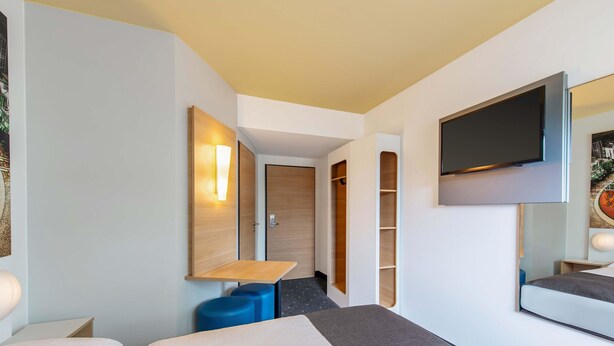A modern hotel room with a bed, a desk, a TV, and a wardrobe. - B&B Hotel Augsburg-Süd (Augsburg)
