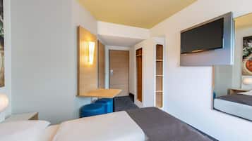 A modern hotel room with a bed, a desk, a TV, and a wardrobe.