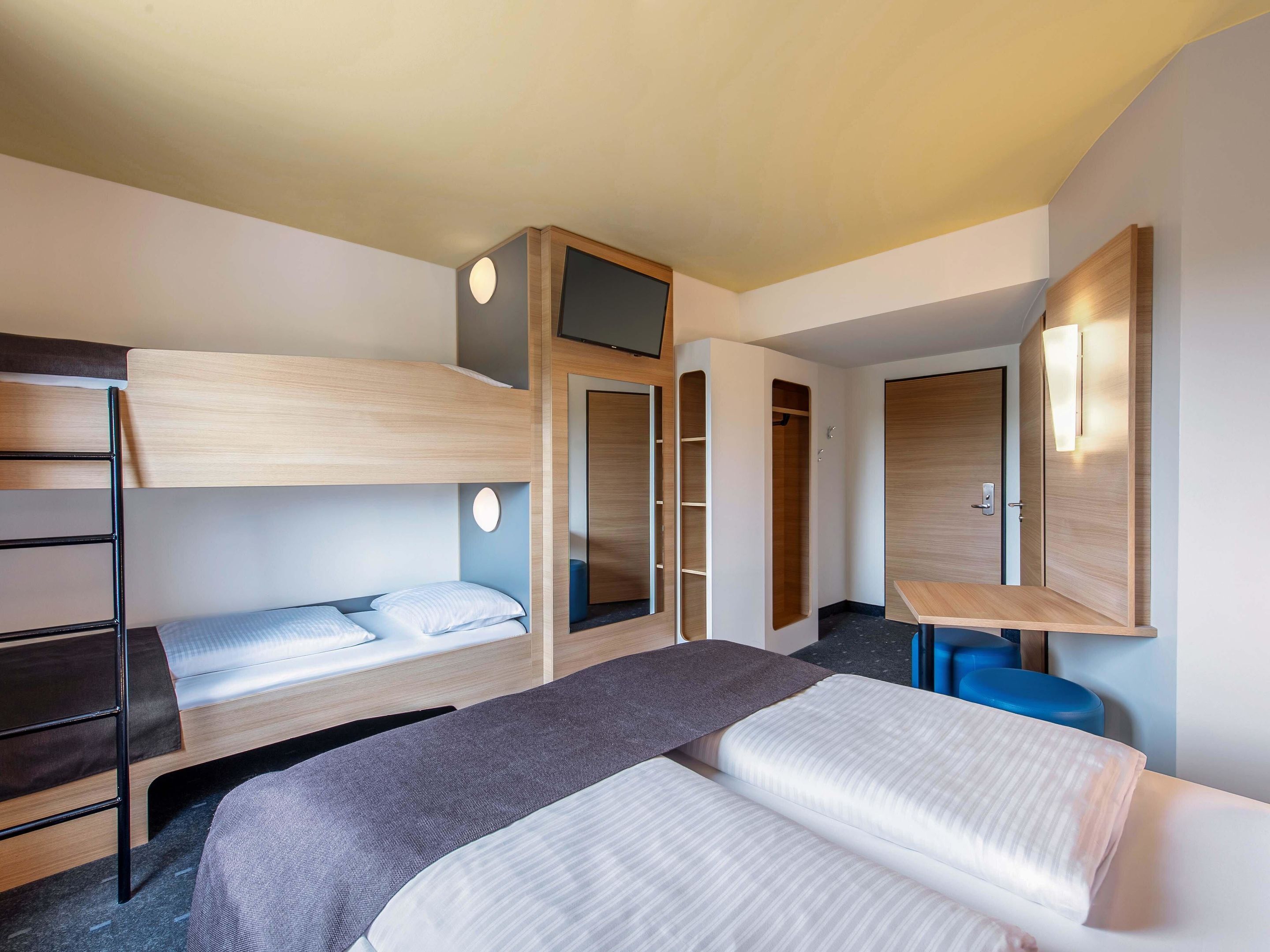 Una habitación de hotel moderna con literas, un escritorio, un armario y un televisor.