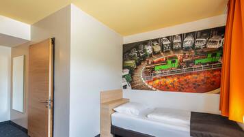 Una habitación de hotel con una cama, un cuadro de trenes, una puerta de madera y piso alfombrado.