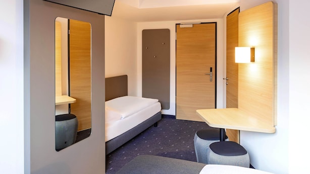 A hotel room with a bed, a desk, a chair, a TV, and a mirror. - B&B Hotel Augsburg-Süd (Augsburg)