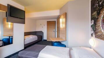 Habitación de hotel con cama, escritorio, silla, televisor y puerta.