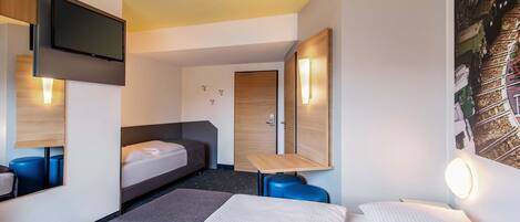 Habitación de hotel con cama, escritorio, silla, televisor y puerta.