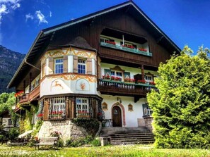 A traditional chalet with a stone foundation, multiple balconies with red flowers, and a mountain backdrop. - Gästehaus Hohe Tannen (Garmisch-Partenkirchen)
