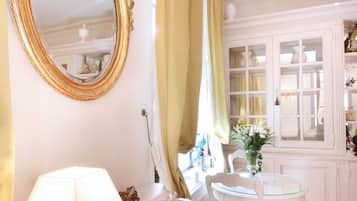 Een kamer met een witte kaptafel, een spiegel met gouden lijst, een witte tafel met een lamp en een stoel.