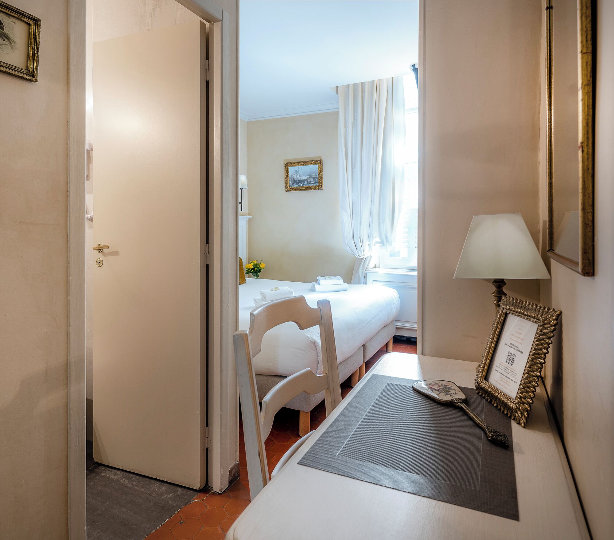Une chambre d’hôtel avec un lit, une chaise, une table avec une lampe et un tableau encadré.