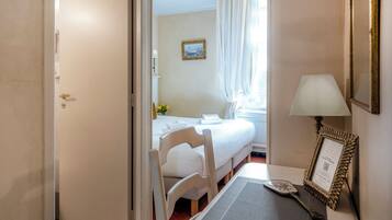 Une chambre d’hôtel avec un lit, une chaise, une table avec une lampe et un tableau encadré.