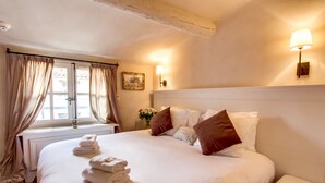 Ein ordentlich bezogenes Bett mit weißen Leinentüchern und braunen Kissen, ein Nachttisch und ein Fenster mit Vorhängen.