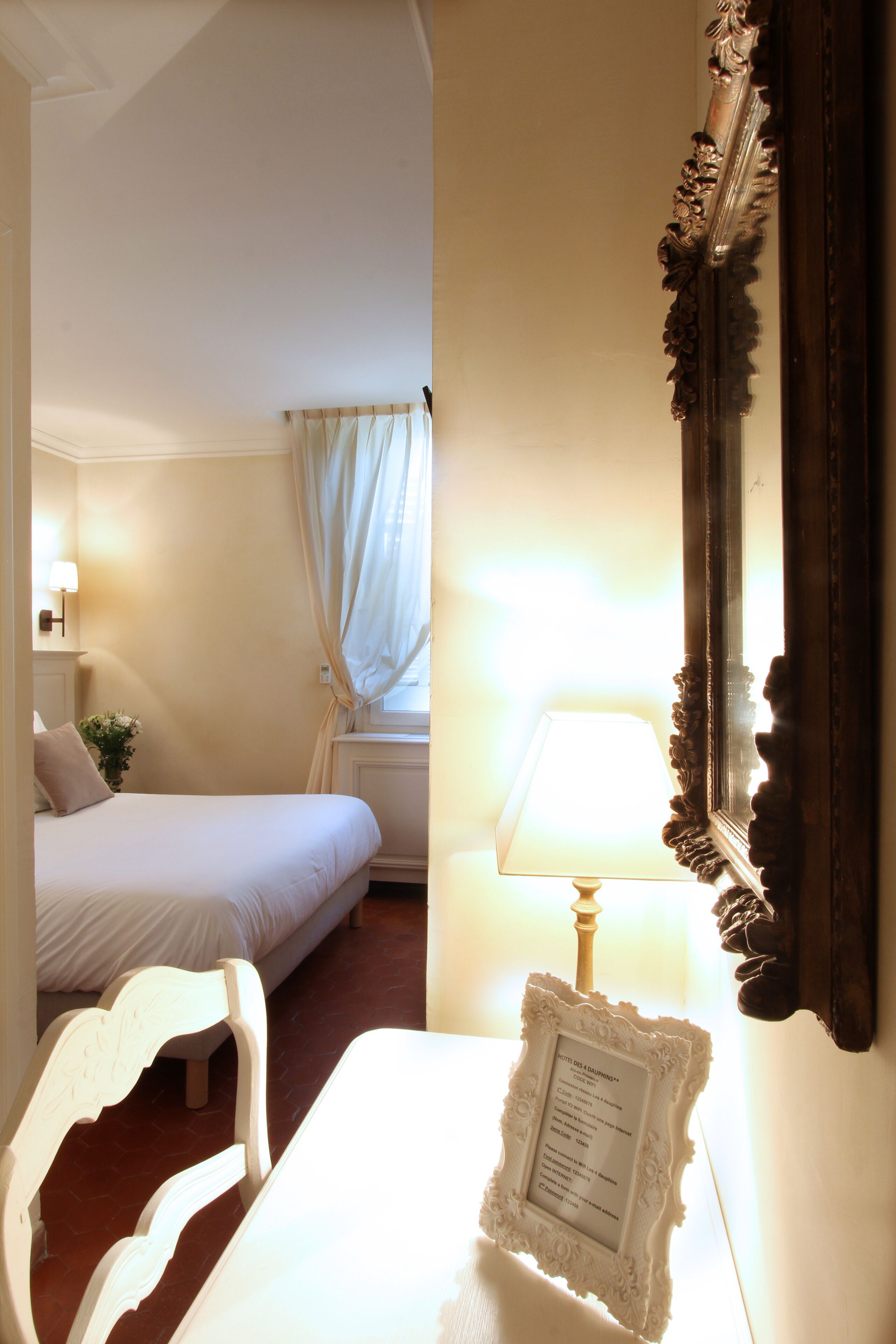 Ein Hotelzimmer mit Bett, Stuhl, Tisch, Lampe, Spiegel und einem Fenster mit Vorhängen.