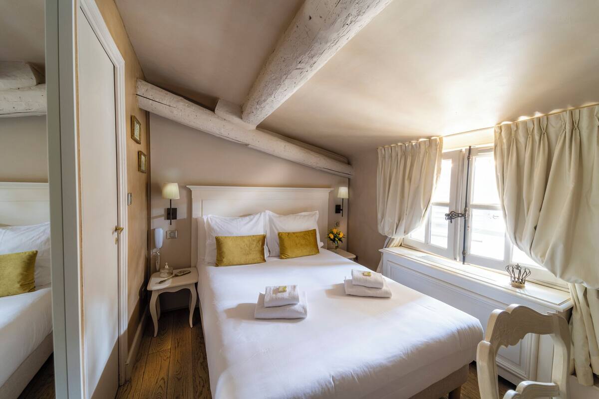 Una habitación de hotel con una cama grande, dos mesitas de noche, una silla y una ventana con cortinas.