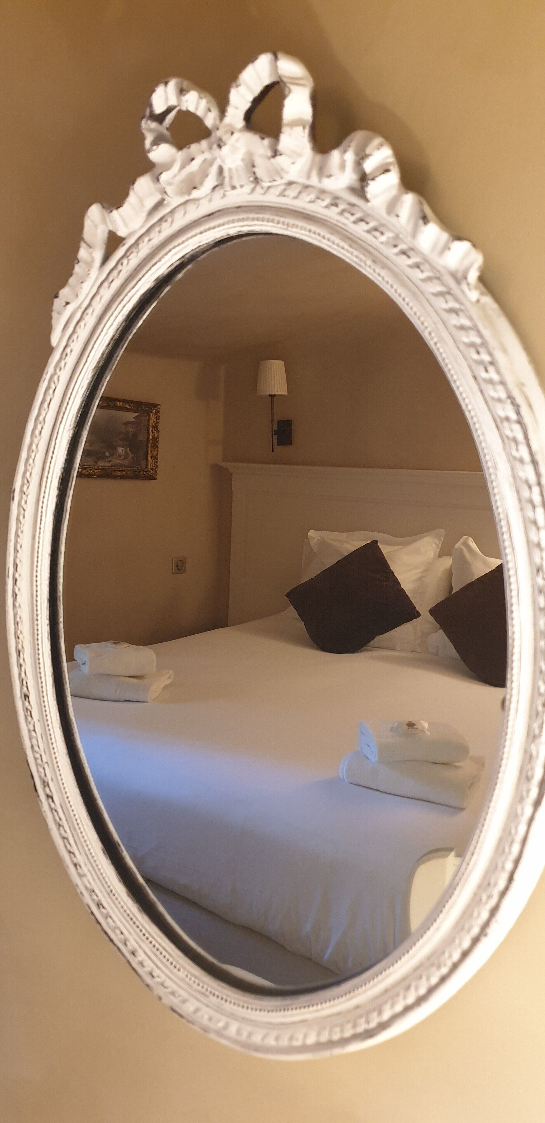 Una camera d'albergo con un grande specchio decorato, un letto rifatto con lenzuola bianche e un quadro appeso al muro.