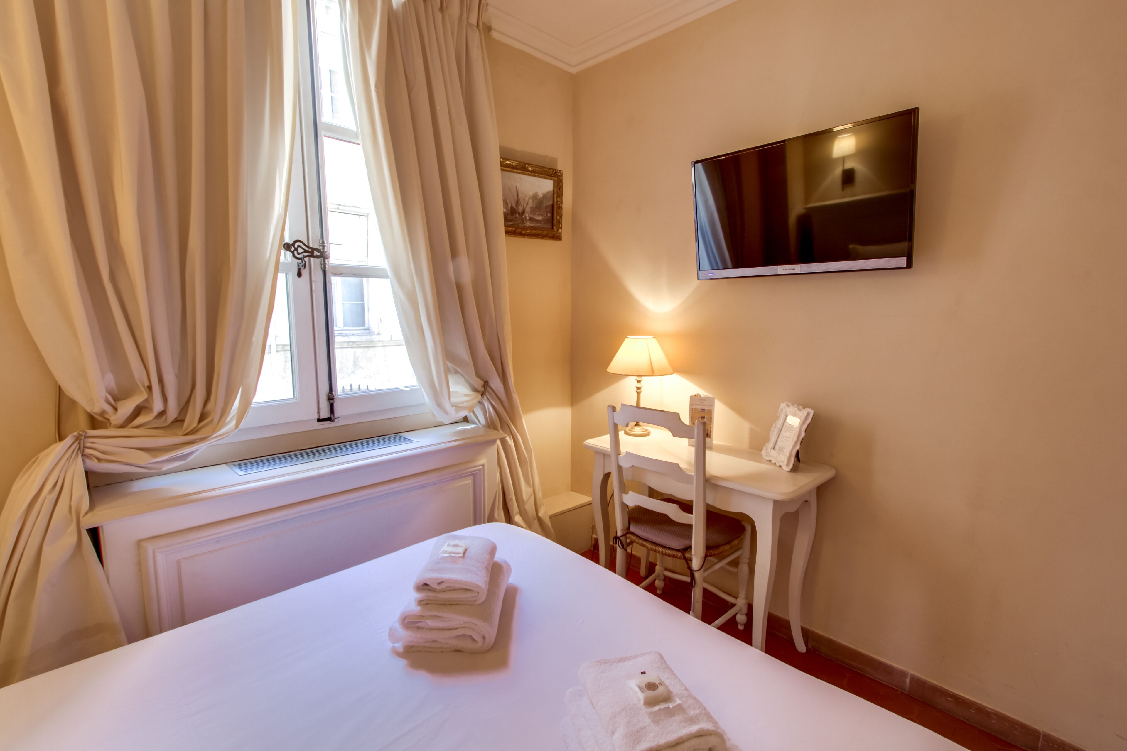 Una habitación de hotel con cama, escritorio, silla, televisor y ventana con cortinas.