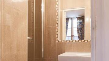 Un baño con ducha envuelta en vidrio, un lavamanos blanco y un espejo con un borde de azulejos decorativos.