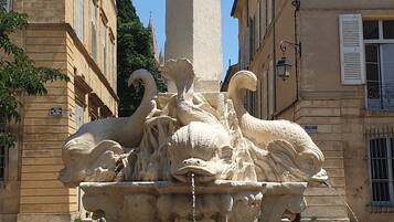 Uma fonte com coluna central e esculturas de cisnes, rodeada por edifícios.