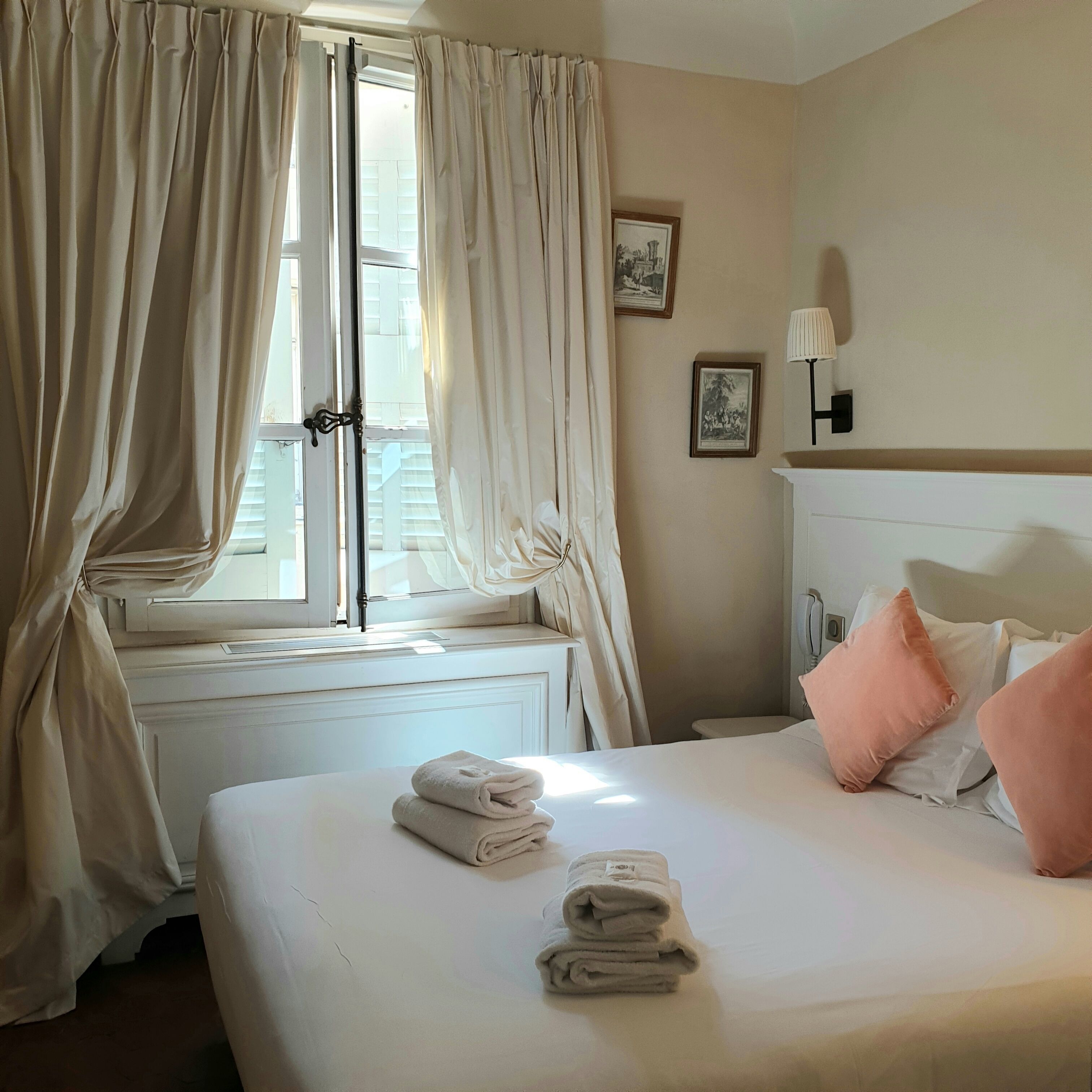 Een hotelkamer met een bed, kussens, een radiator en gordijnen.