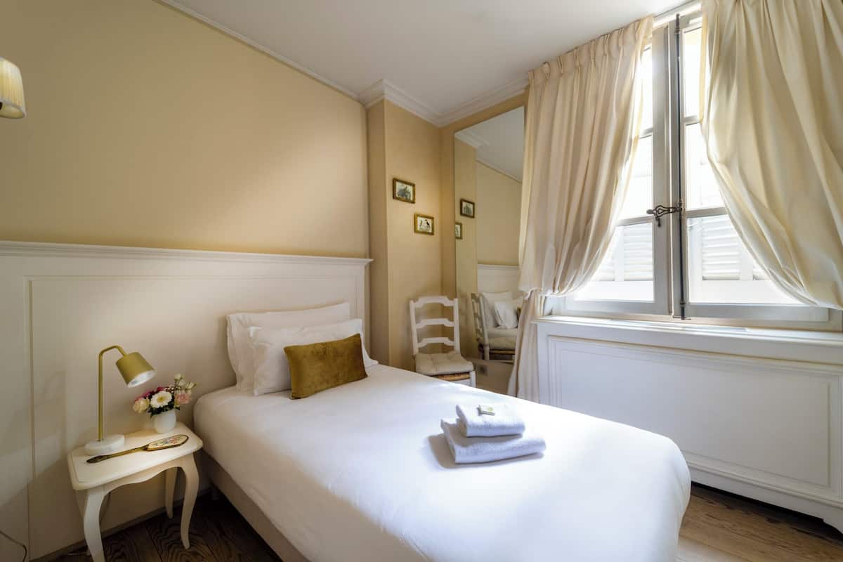 Habitación de hotel ordenada con cama, mesita de noche, lámpara y ventana con cortinas.