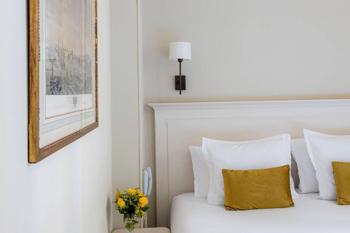 Una habitación de hotel con una cama grande, una mesita de noche con un florero y un cuadro en la pared.