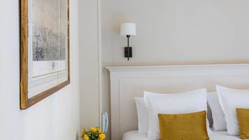 Une chambre d’hôtel avec un grand lit, une table de chevet ornée d’un vase de fleurs et un tableau encadré au mur.