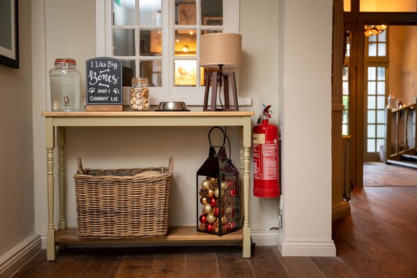 A wooden console table with a sign, jars, a lamp, a basket, and a fire extinguisher.
