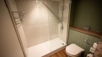 Een moderne badkamer met een douche met glazen wand, witte betegelde wanden, een houten vloer en een groene accentmuur.