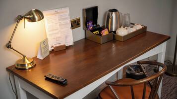 A hotel desk with a lamp, remote control, menu, and a tray with a coffee pot and glasses.