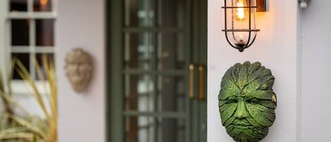 A building entrance with a green door, a wall-mounted lantern, and a decorative leaf-shaped plaque.
