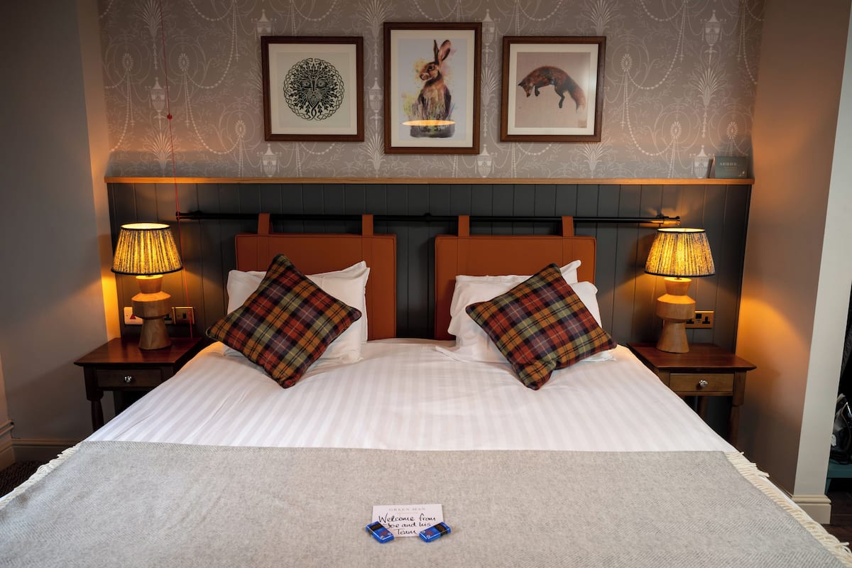 A neatly made bed with plaid pillows, two bedside lamps, and framed artwork on the wall.