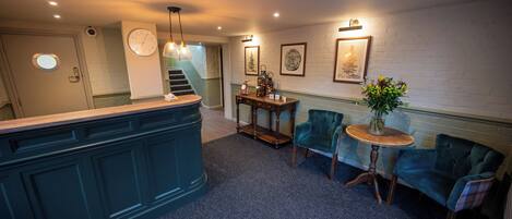 A lobby with a reception desk, a staircase, a round wooden table with chairs, and framed artwork on the walls.