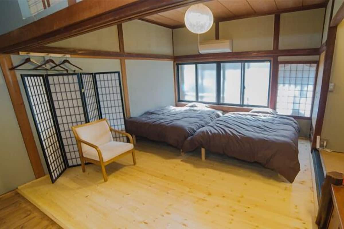Perinteinen japanilaistyylinen huone, jossa on tatamimatto, futon-patja, puinen tuoli ja liukuvat shoji-ovet.