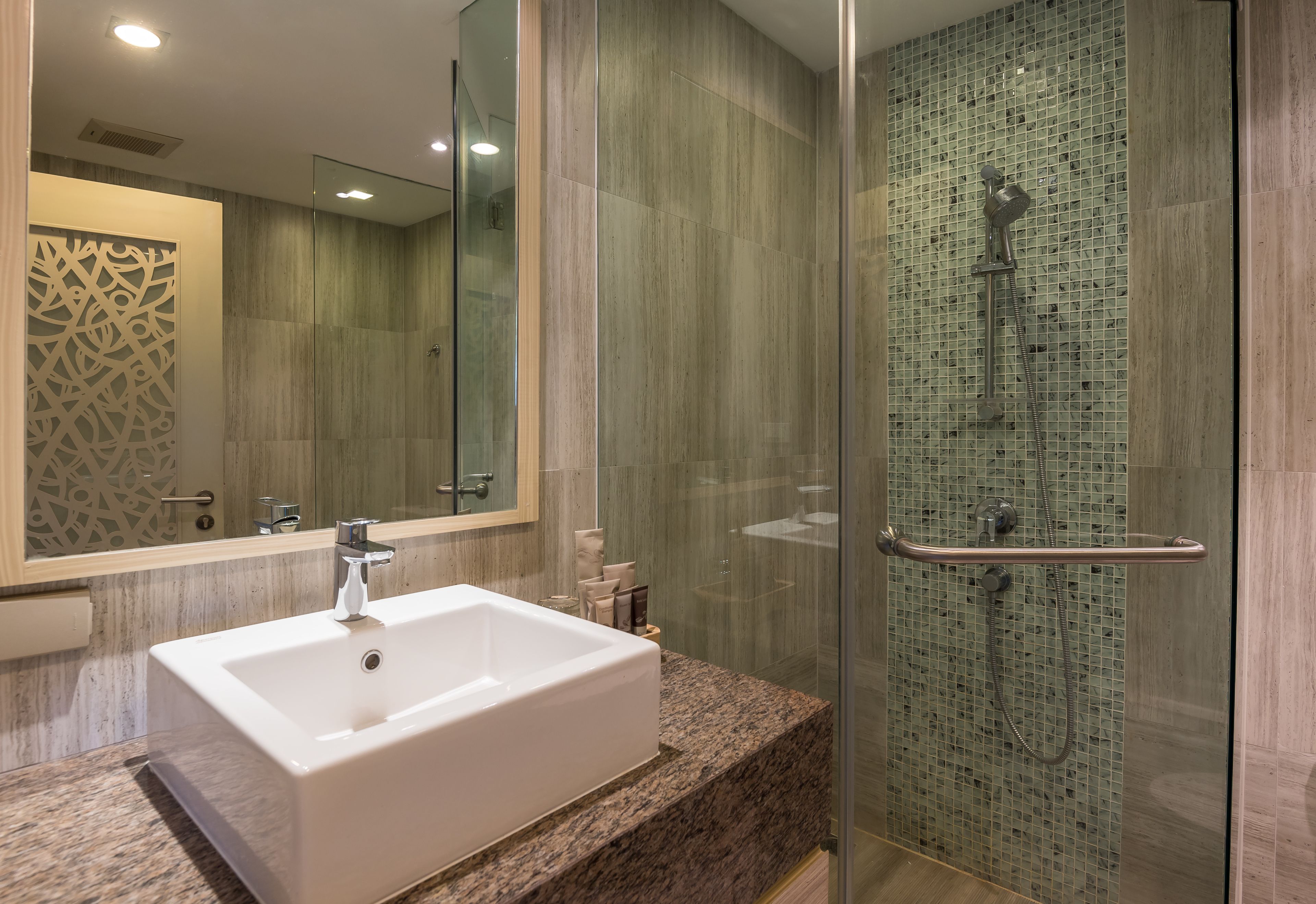 Un baño moderno con un lavamanos grande de color blanco, cabina de ducha con mampara de vidrio y un panel decorativo en la pared.