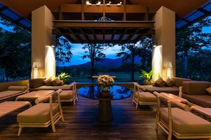 A modern outdoor lounge area with a round table, cushioned seating, and a view of a natural landscape.
