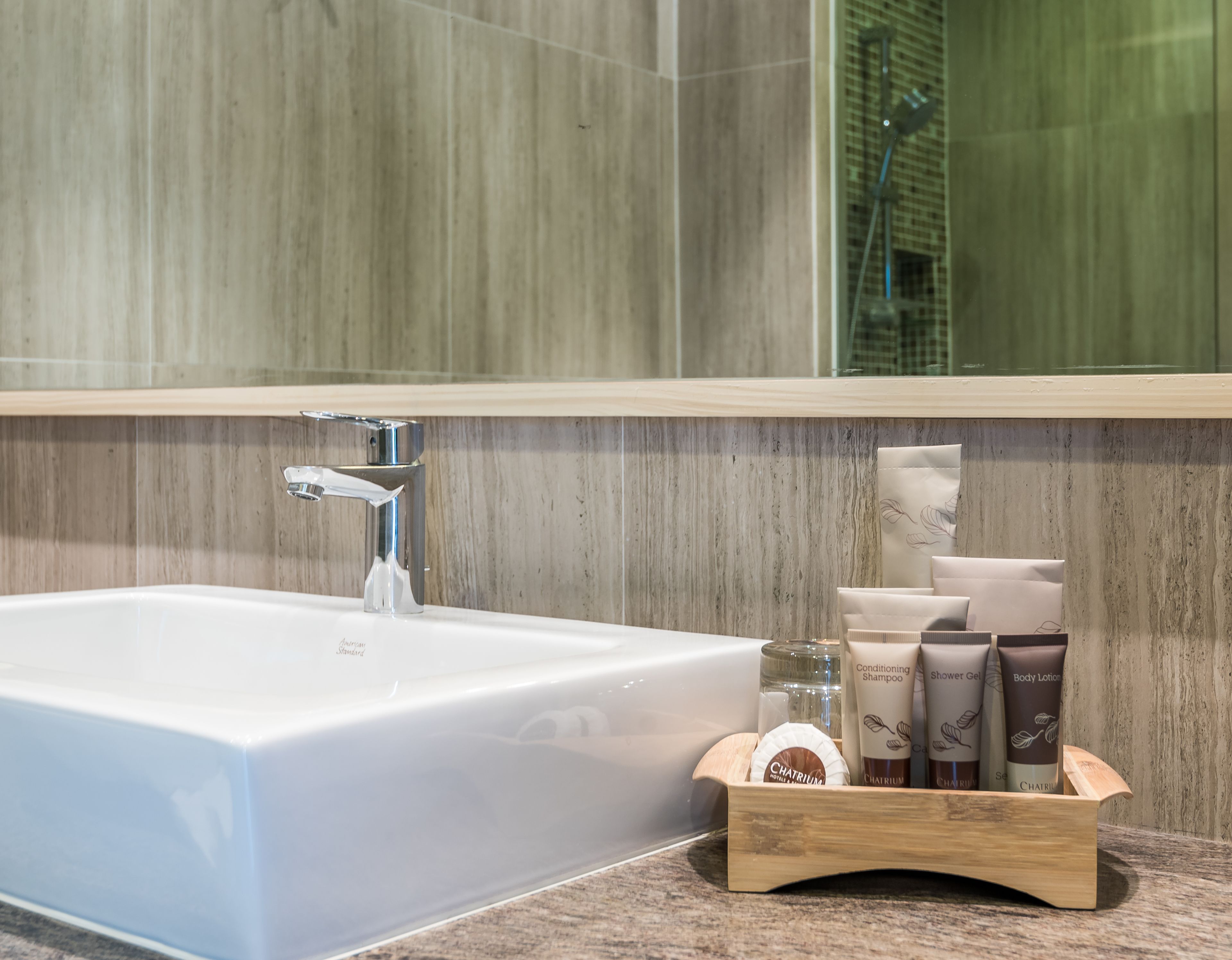 A bathroom with a white sink, a chrome faucet, and a wooden vanity with toiletries.