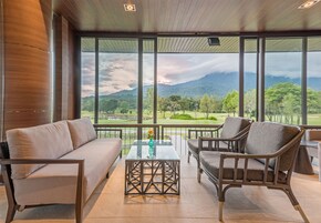 A modern room with a sofa, armchair, and table, large windows with a view of a golf course and mountains.